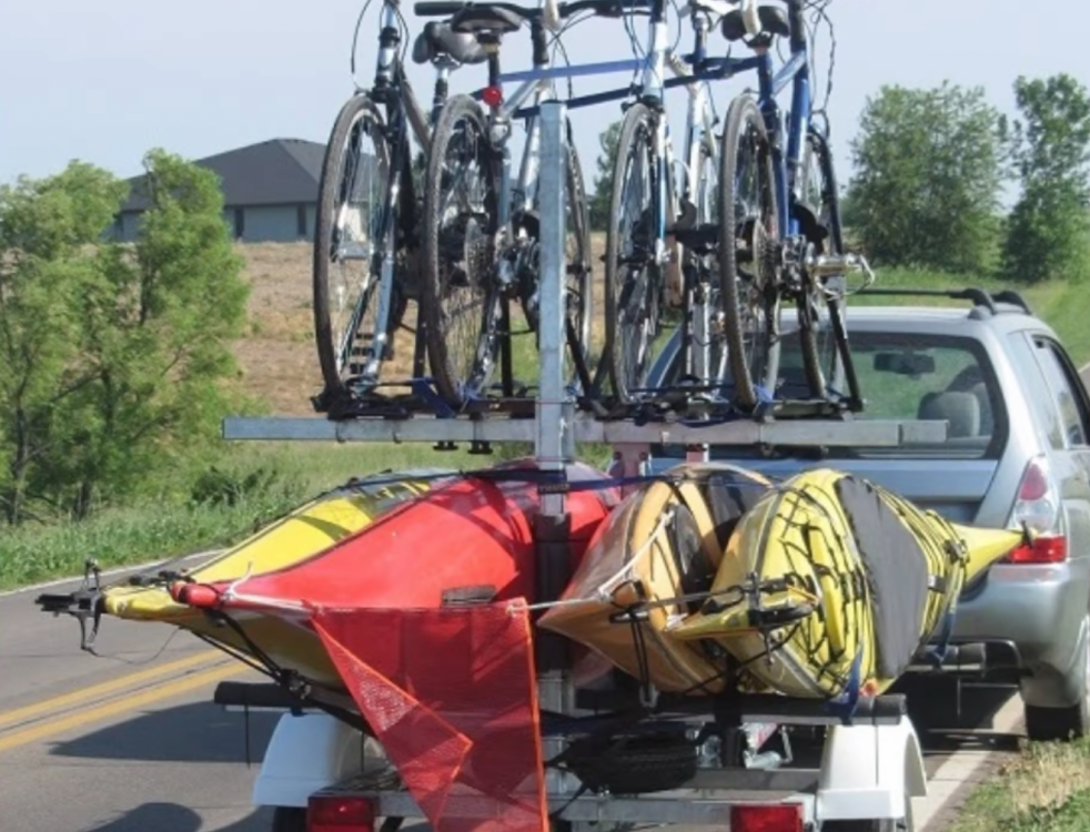 4 bikes and 4 kayaks on a trailer being hauled behind a car.